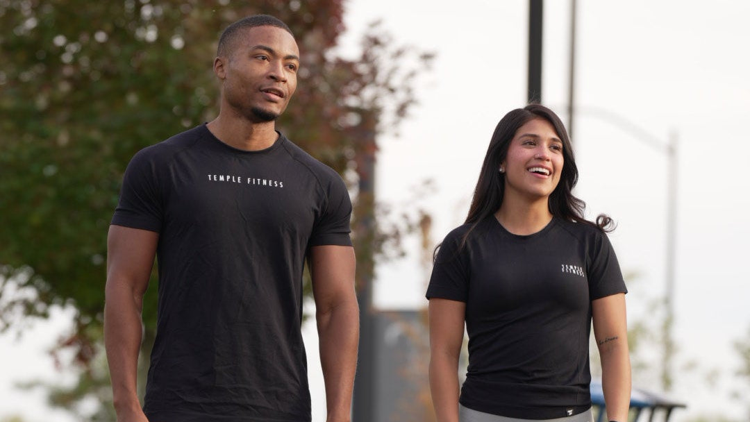 Two people standing on a road with trees and grass in the background
