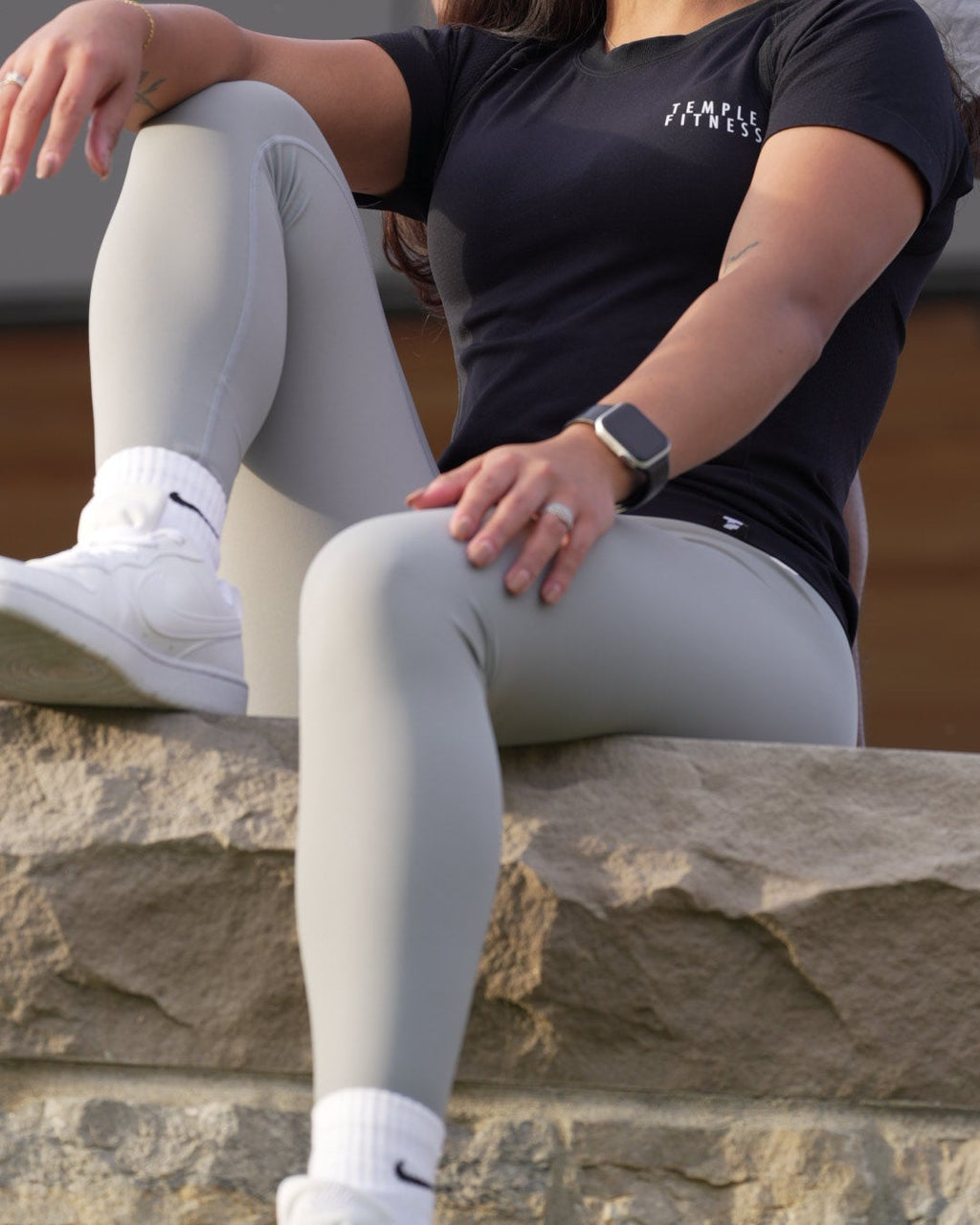 Person wearing a black shirt and gray leggings sitting on a rock ledge.