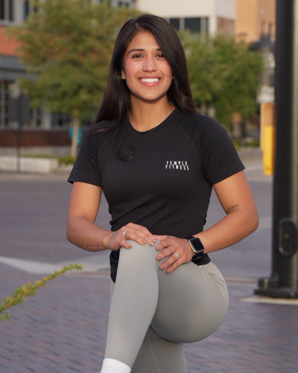 Person in black t-shirt and gray leggings standing outdoors with buildings in the background